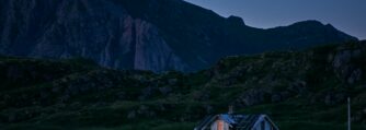 A house with lights on sitting in the middle of a landscape as the night draws in