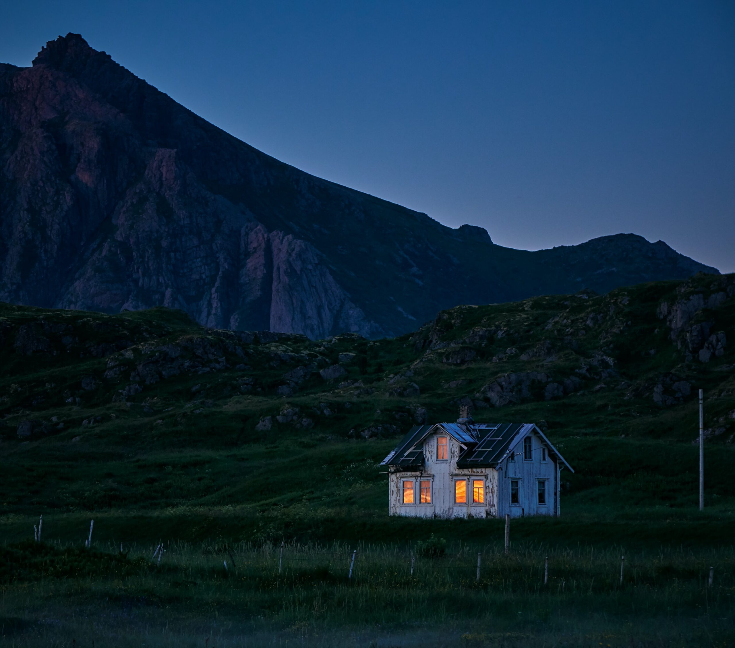 A house with lights on sitting in the middle of a landscape as the night draws in